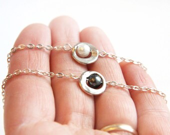 May include: Two silver chains with a circle pendant on each. One pendant has a white pearl and the other has a black pearl.