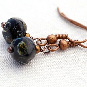 May include: A pair of black and gold earrings with copper wire and hooks. The earrings feature black glass beads with gold flecks.
