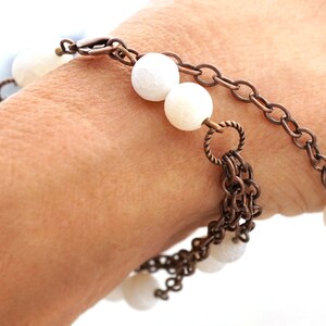 May include: A copper chain bracelet with white agate beads. The bracelet has a lobster clasp closure and a decorative charm.
