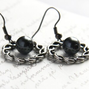 May include: A pair of silver earrings with a black bead on each. The earrings are made of a twisted chain design.