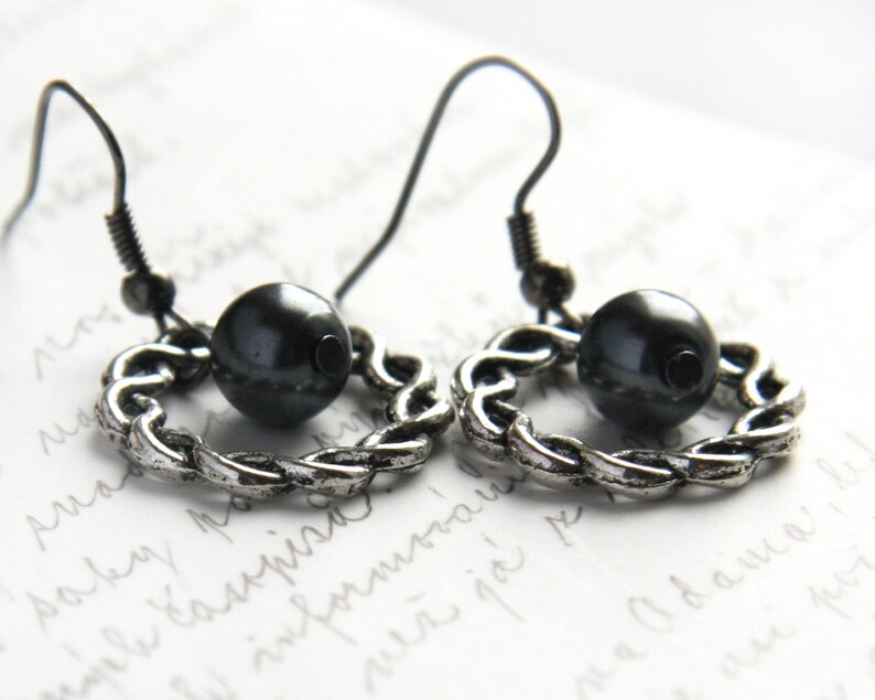May include: A pair of silver earrings with a black bead on each. The earrings are made of a twisted chain design.