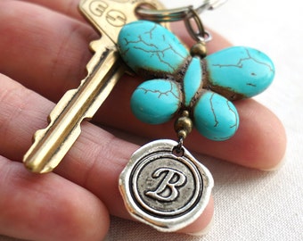 May include: A turquoise butterfly charm with a silver initial "B" charm attached to a gold key and a silver key ring.