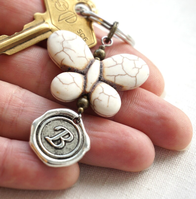 May include: White butterfly charm with a brown wax seal charm with the letter "B" on a gold key chain.