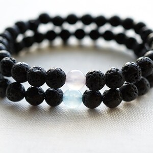 Könnte beinhalten: Ein doppelreihiges Armband aus schwarzen Lavasteinen mit zwei Akzentperlen, einer hellrosa und einer hellblauen.