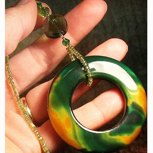 May include: A green, orange, and black agate pendant in the shape of a ring, hanging from a gold chain with green and clear beads.