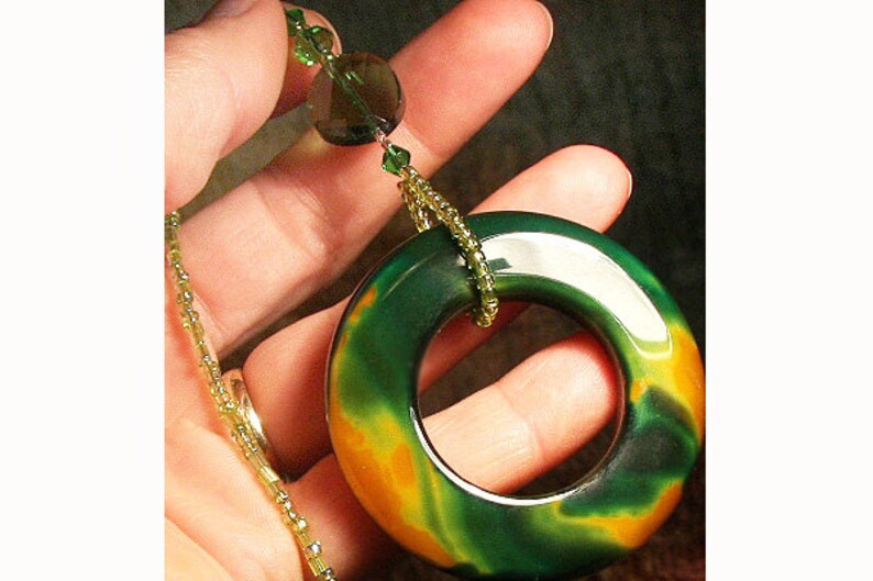 May include: A green, orange, and black agate pendant in the shape of a ring, hanging from a gold chain with green and clear beads.