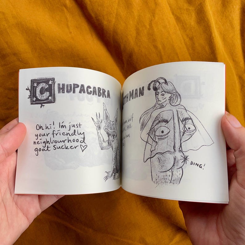 May include: An open book with illustrations of a chupacabra and a mothman. The chupacabra is a creature with large ears and sharp teeth. The mothman is a humanoid figure with large wings. The text on the page reads "Oh hi! I'm just your friendly neighbourhood goat sucker." and "Mothman".