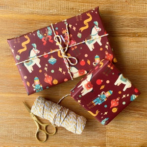 May include: Two red and white patterned gift wrap rolls with a white twine string and gold scissors. The gift wrap features a festive Christmas design with nutcrackers, horses, and ornaments.