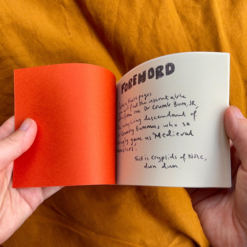 May include: A small, white book with a black handwritten foreword. The text reads "Foreword. Within these pages you will find the inscrutable story from one Dr Crumb Bum, Jr, the only living descendant of Cumby Bummus who so lovingly gave us Medieval monsters. This is cryptids of Norc, dun dun."