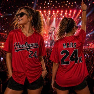 May include: Two people wearing red baseball jerseys with the text "Hooligans 24K" and "Mars 24K" in black. The jerseys have a button-down front and are paired with black shorts. The background shows a concert stage with bright lights.