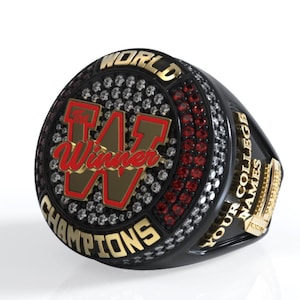 Puede incluir: Un anillo de campeonato negro y dorado con acentos rojos y blancos. El anillo presenta la palabra "WORLD" en la parte superior, "CHAMPIONS" en la parte inferior y una gran "W" con la palabra "Winner" en su interior. El anillo también tiene las palabras "YOUR COLLEGE NAMES" en el lateral.