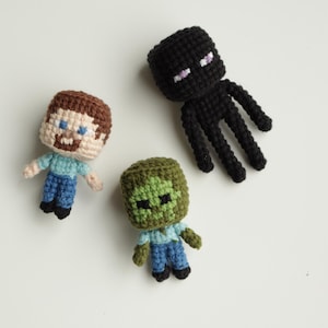 Könnte beinhalten: Drei gehäkelte Minecraft-Charaktere: Steve, ein Zombie und ein Enderman. Steve hat braunes Haar und einen Bart. Der Zombie ist grün. Der Enderman ist schwarz mit lila Augen. Alle tragen blaue Hemden und Jeans.