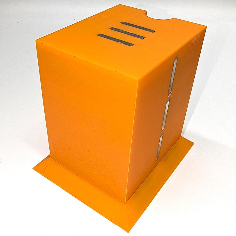 May include: Bright orange rectangular box with three horizontal slits on top and three vertical slits on the side. The box has a base and a notch cut out of the top. The object is made of a solid material.