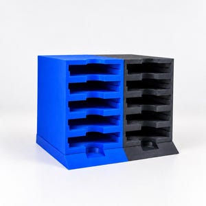 May include: A dual-section desktop organiser featuring a bright blue side and a matte black side. Each section contains five horizontal slots with curved cutouts for easy access, designed for stacking and storing flat items in a compact unit.