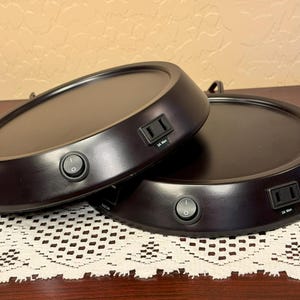 May include: Two round, black, wooden bases with electrical outlets and switches. The bases are stacked on top of each other.