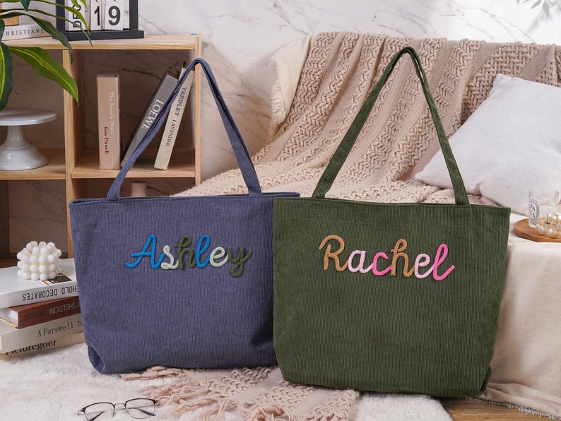 May include: Two corduroy tote bags, one blue and one green, with embroidered names. The blue bag says "Ashley" in blue, green, and white thread. The green bag says "Rachel" in tan and pink thread. Both have long handles.