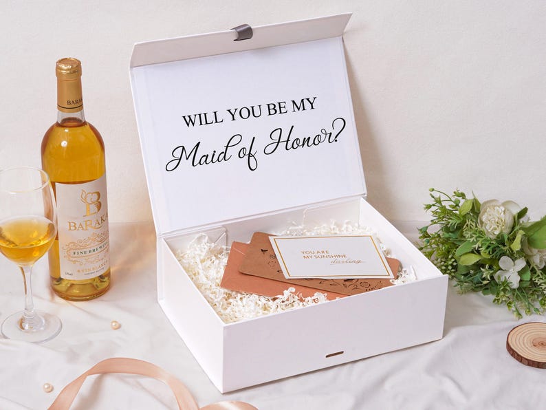 Pu&ograve; includere: Una scatola regalo rettangolare bianca con coperchio incernierato che presenta il testo stampato in nero WILL YOU BE MY Maid of Honor? La scatola &egrave; riempita con carta sminuzzata bianca, inserti in cartoncino marrone e un cartoncino bianco.