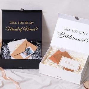 Pu&ograve; includere: Una scatola regalo nera con testo dorato Will You Be My Maid of Honor e una scatola bianca con testo nero Will You Be My Bridesmaid. Entrambe le scatole contengono carta sminuzzata, buste marroni e piccoli biglietti.