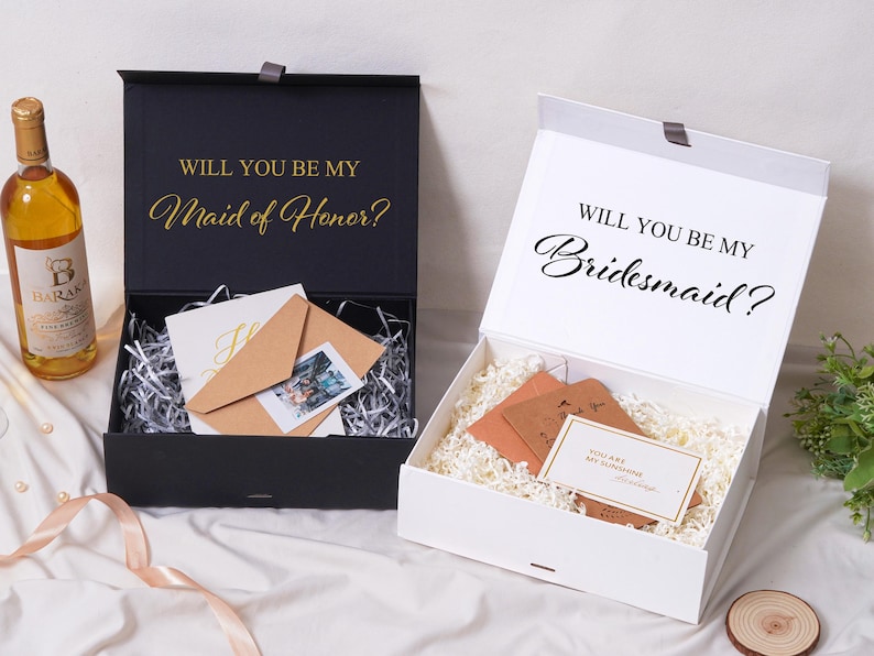 Pu&ograve; includere: Una scatola regalo nera con testo dorato Will You Be My Maid of Honor e una scatola bianca con testo nero Will You Be My Bridesmaid. Entrambe le scatole contengono carta sminuzzata, buste marroni e piccoli biglietti.