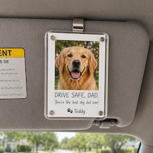 May include: A clear, rectangular car visor accessory with a photo of a golden retriever. The text "DRIVE SAFE, DAD. You're the best dog dad ever!" is printed below the photo, along with the name "Teddy" and paw prints.