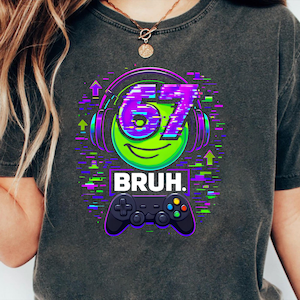 Könnte beinhalten: Dunkelgraues T-Shirt mit einem Grafikdesign, das ein grünes Smiley-Gesicht mit lila Kopfhörern mit der Zahl "67" und dem Wort "BRUH" zeigt. Unten im Design befindet sich ein schwarzer Gamecontroller.