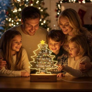 Puede incluir: Una familia observa una lámpara con forma de árbol de Navidad iluminada. La lámpara está personalizada con nombres y el texto "The James Family 2025". Se apoya en una base de madera con la inscripción "Custom Text" debajo.