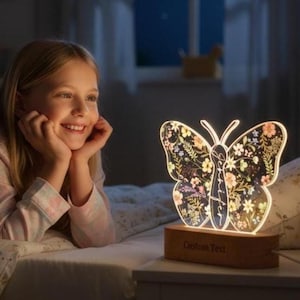 Könnte beinhalten: Ein schmetterlingsförmiges Nachtlicht mit floralem Design und Holzsockel. Das Licht ist eingeschaltet und beleuchtet die filigranen Details der Schmetterlingsflügel. Auf dem Sockel steht "Custom Text".