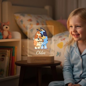 Könnte beinhalten: Eine klare Acryl-Nachtlampe mit einem Cartoon-Bild von drei Figuren in Orange und Blau, mit dem Namen "Chloe" und den Worten "Custom Text" auf der Basis. Das Licht steht auf einem kleinen Holztisch.