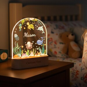 May include: A decorative night light with an arched acrylic panel featuring an underwater scene with a seahorse, turtle, dolphin, whale, and octopus. The name "Mason" is displayed, with the words "Custom Text" below. The light sits on a wooden base.
