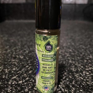 May include: A green and black roll-on bottle with a label that says "100% Pure Oil" and "Never Diluted Hypoallergenic". The label also includes the text "Reference to brand names are strictly for comparison" and "Ingredients: Fragrance Blend of Oil".