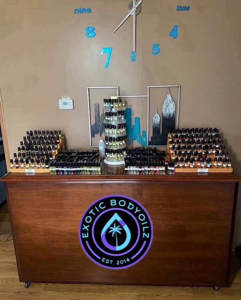 May include: A wooden counter with a variety of small glass bottles filled with liquid. The counter has a sign that says "Exotic Body Oils Est. 2014".