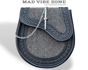 Puede incluir: Un sporran de tweed gris y negro con cierre de pasador y cadena plateada. La parte delantera presenta un patrón de espiga y bordes decorativos. El texto "MAD VIBE ZONE" y "Grey Tweed Pin Lock Sporran" están en la parte superior.