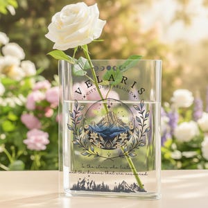 Puede incluir: Un jarr&oacute;n de vidrio transparente con el texto "VELARIS CITY OF STARLIGHT" y un dise&ntilde;o de monta&ntilde;a, que sostiene una rosa blanca. El jarr&oacute;n tiene agua dentro y el texto "To the stars who listen and the dreams that are answered".