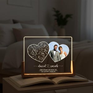 May include: A personalised LED night light with a wooden base. It features two heart-shaped cutouts, one with a star map and the other with a couple's photo. The names "David & Sarah" and the date are displayed.