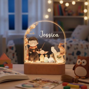 May include: A wooden-based night light featuring a cartoon illustration of a wizarding theme. The light has a curved, clear acrylic panel with the name "Jessica" and images of characters, potions, and an owl. The base is made of wood.