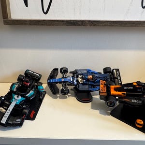 May include: A collection of detailed model Formula 1 race cars in various colors, including red, black, blue, and orange. The cars are displayed on a white surface, showcasing their intricate designs and sponsor logos. The image captures the essence of motorsport.