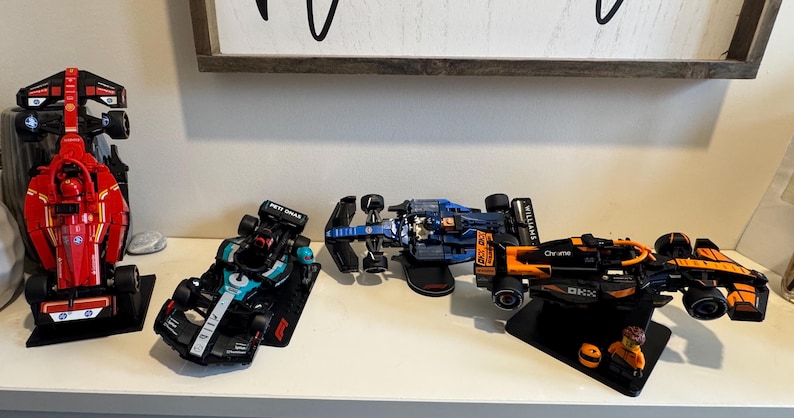 May include: A collection of detailed model Formula 1 race cars in various colors, including red, black, blue, and orange. The cars are displayed on a white surface, showcasing their intricate designs and sponsor logos. The image captures the essence of motorsport.