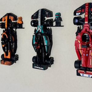 May include: Four toy Formula 1 race cars in blue, orange, teal, and red, mounted on a white wall. Each car has a unique design and is accompanied by a small figurine. The cars are displayed on small black shelves.