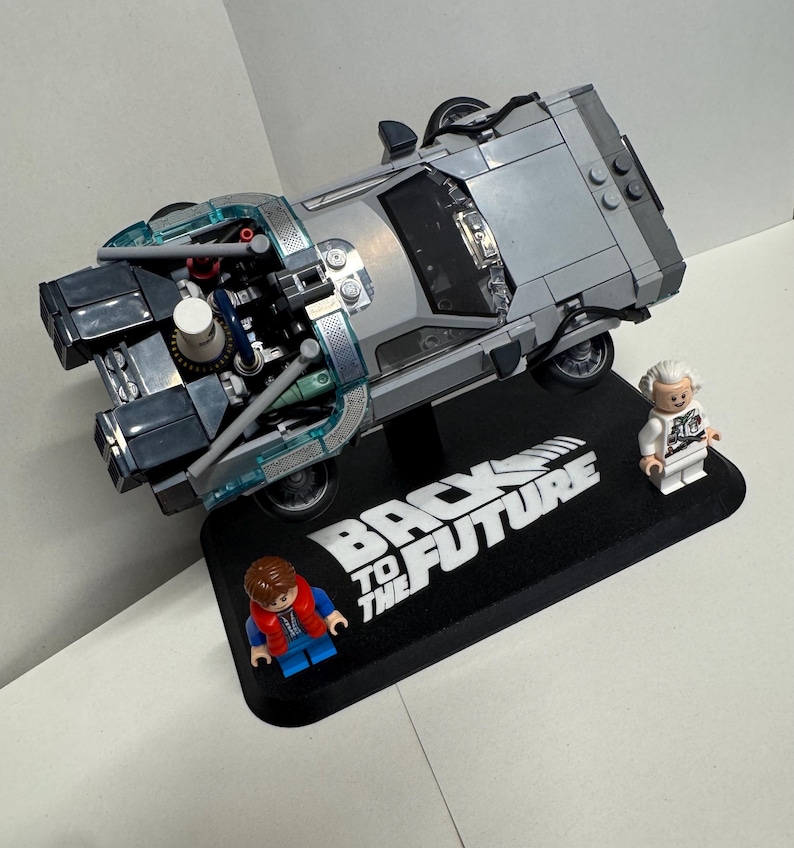 May include: A silver Lego DeLorean time machine model with detailed engine components, displayed on a black base with "Back to the Future" text. Includes Lego figures of Marty McFly and Doc Brown.