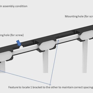 May include: A black metal bracket with a white plastic insert. The bracket has a mounting hole for a screw and a feature to locate it to other brackets. The text "Back Mounted brackets - In assembly condition" is visible in the image.