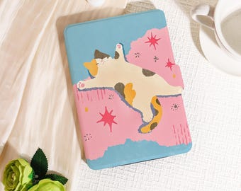 May include: A light blue tablet case featuring a whimsical illustration of a relaxed calico cat. The case has a pink section with star accents and a magnetic closure. The cat is white, brown, and orange.