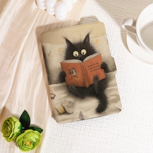 May include: A black cat illustration on a tablet case, reading a book titled "How to be Very Loud at Night." The case has a light beige background with a bed scene, including a pillow, blanket, and a pair of slippers.