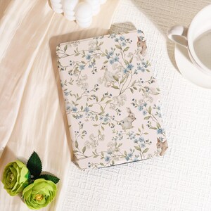 May include: A light pink tablet case featuring a floral and bunny design. The pattern includes blue flowers, green leaves, and illustrations of rabbits and a duck. The case is rectangular and appears to be made of a soft material.