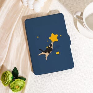 Könnte beinhalten: Eine marineblaue Tablet-Hülle mit einer skurrilen Illustration einer schwarz-weißen Katze, die nach einem großen gelben Stern greift. Zusätzliche kleinere gelbe Sterne sind auf der Hülle verstreut. Mit Magnetverschluss.