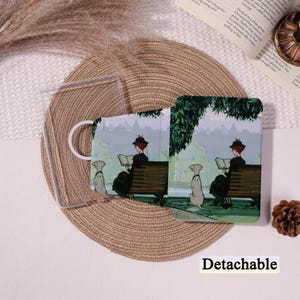 Könnte beinhalten: Eine transparente, abnehmbare Handyhülle und eine passende Gesichtsmaske. Die Maske zeigt eine Vintage-Illustration einer Person, die auf einer Parkbank mit einem Hund liest. Hülle und Maske sind aufeinander abgestimmt.