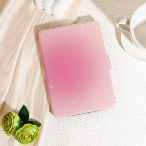 Pode incluir: Uma capa rosa para tablet com um design gradiente, que transita de um rosa mais escuro no topo para um rosa mais claro na parte inferior. Pequenos detalhes brancos em forma de estrela estão espalhados pela superfície. A capa tem um fecho magnético.