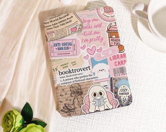 May include: A pink and white book cover adorned with stickers and text. Stickers feature hearts, a ghost reading, and the phrase "buy me books and tell me I'm pretty." The cover also displays the word "booktrovert."