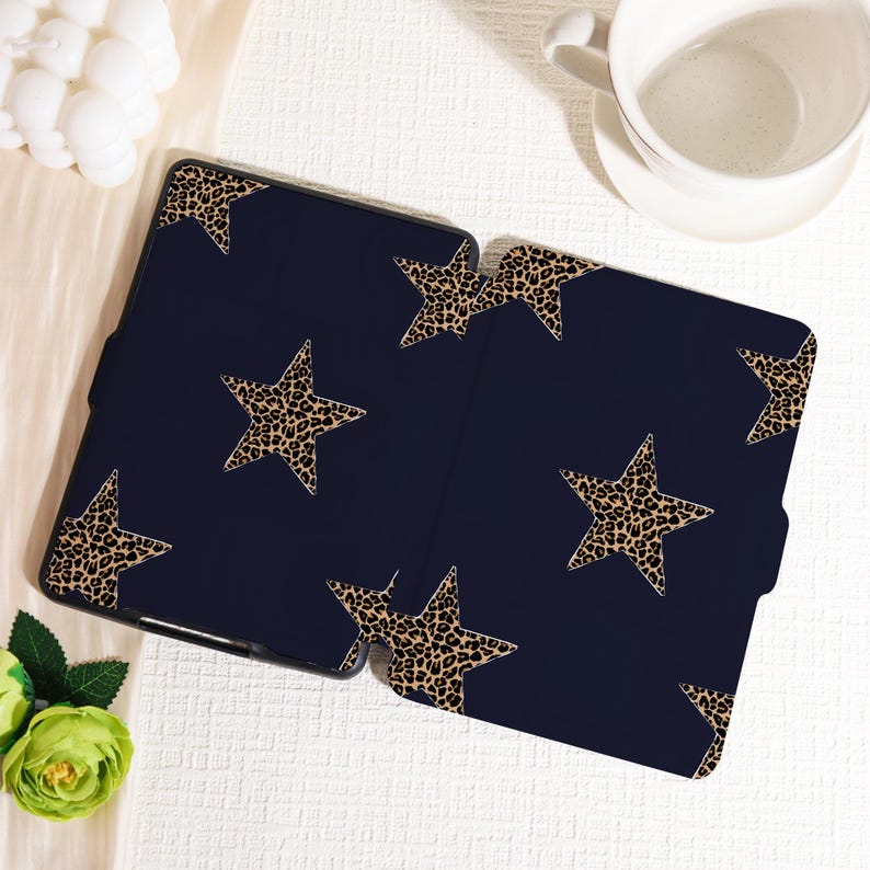 May include: Navy blue tablet case with a leopard print star pattern. The case is open, revealing the interior. The stars are a tan color with black spots. The case is on a white surface with a white coffee cup.