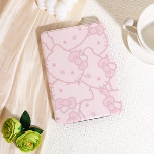Puede incluir: Una funda rosa para tableta con un patrón repetido de caras y lazos de Hello Kitty. La funda es de color rosa claro con un contorno rosa más oscuro del personaje. La funda es rectangular y tiene una superficie lisa.