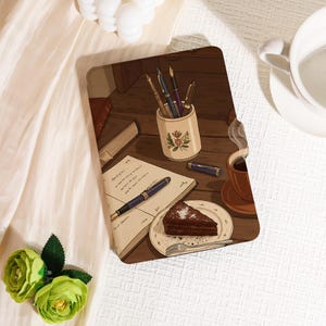 May include: A decorative tray featuring a cozy scene with a cup of coffee, a slice of chocolate cake, and a notebook with a fountain pen. A pen holder with several pens and a book are also visible.